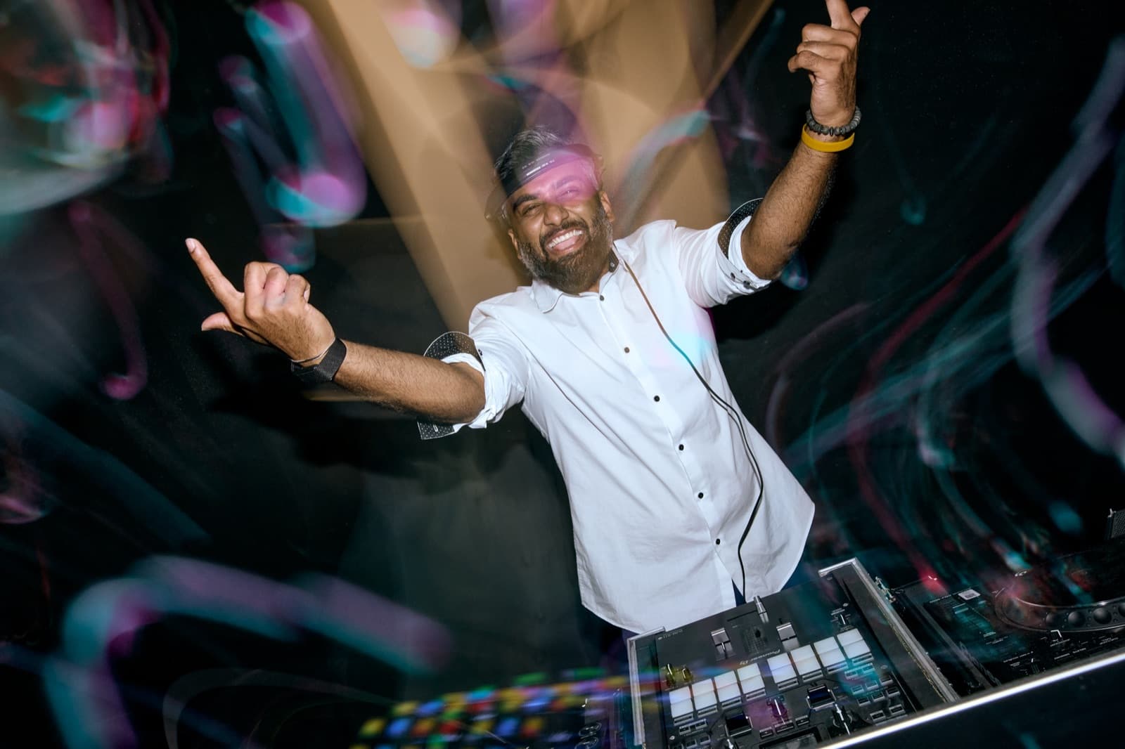 DJ throwing both arms up behind a Pioneer controller as coloured light trails streak across the frame